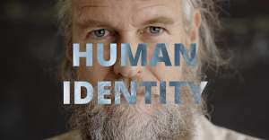 close up of a man's face with a greay beard and words human identity displayed over the center